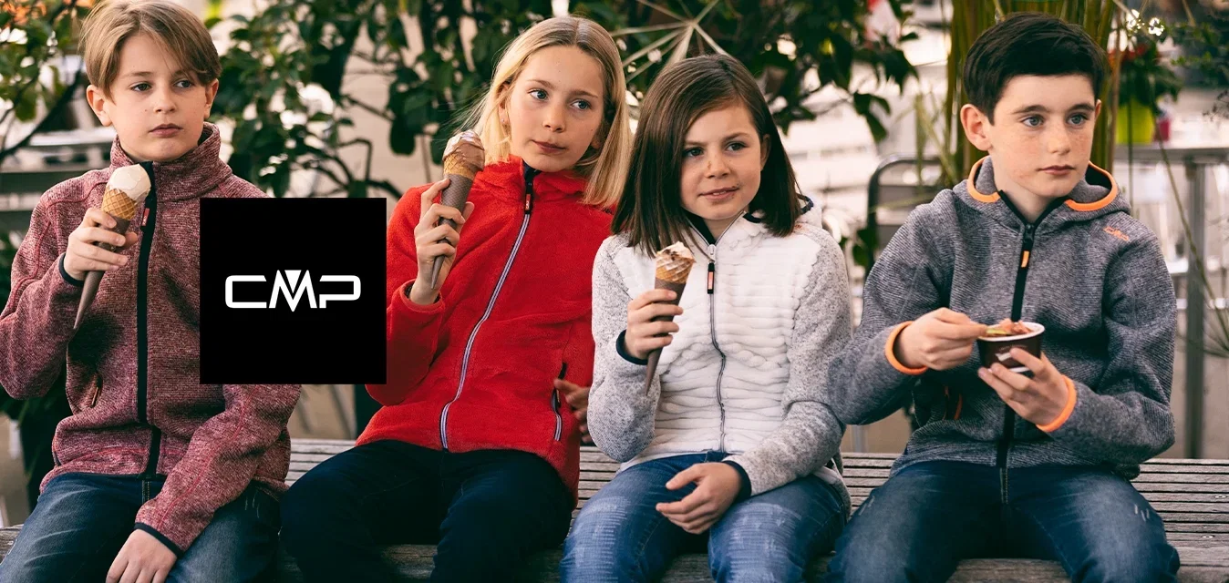 Vier Kinder sitzen auf einer Holzbank und halten Eistüten. Sie tragen Jacken: eine rote Fleecejacke, eine weiße gesteppte Jacke und zwei graue Zip-Jacken.