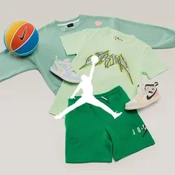 Grüner Sweatshirt, hellgrünes Grafik-T-Shirt, grüne Shorts, zwei weiße Sneakers und ein orange-blauer Nike-Basketball auf hellem Hintergrund.