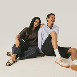 Zwei Personen sitzen auf dem Boden und lächeln, wobei eine Person den Arm auf die Schulter der anderen legt.