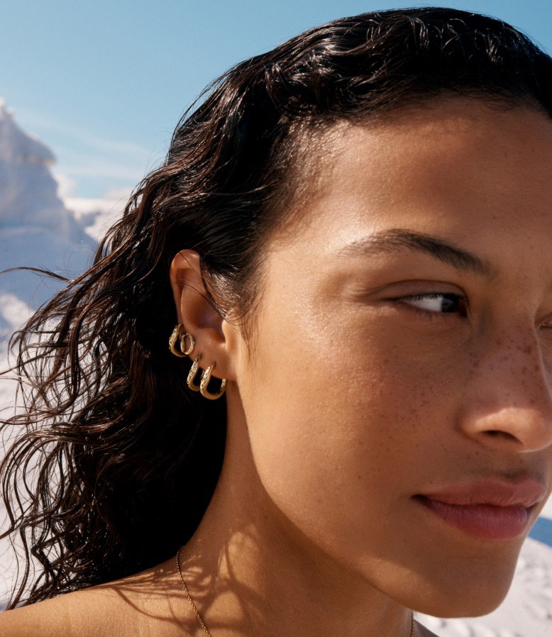 A model looks away and wears a stack of 14k gold-plated hoops.