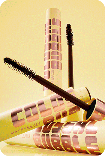 Lifestyle image of Colossal Bubble Mascara tubes laying down and one open displaying the brush with a yellow background