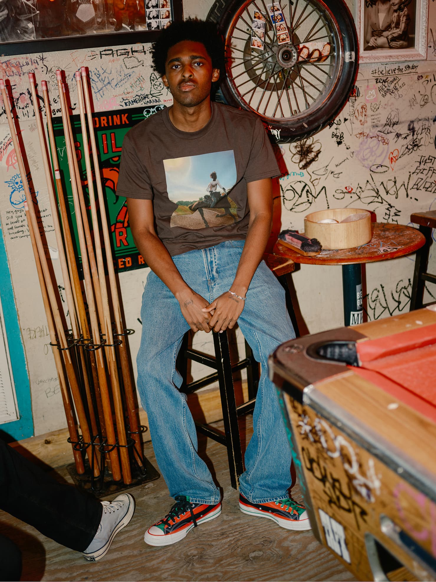 Model sitting in a bar chair wearing Gem Hale collection Tshirt