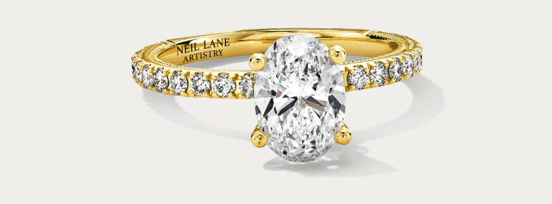 An oval diamond engagement ring in yellow gold with pavé-set diamonds.