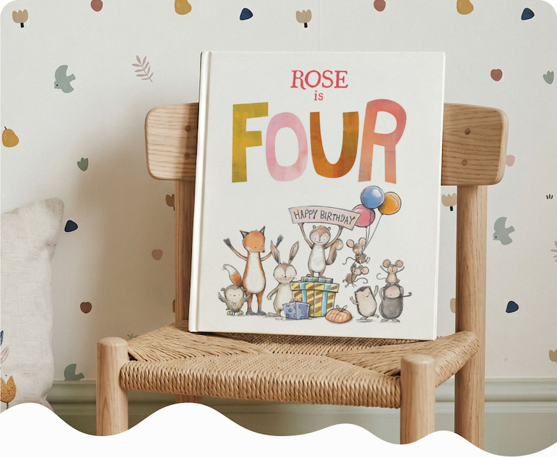 A personalised birthday story book with the name Rose on the cover, resting on a wooden children's chair against a patterned wallpaper background