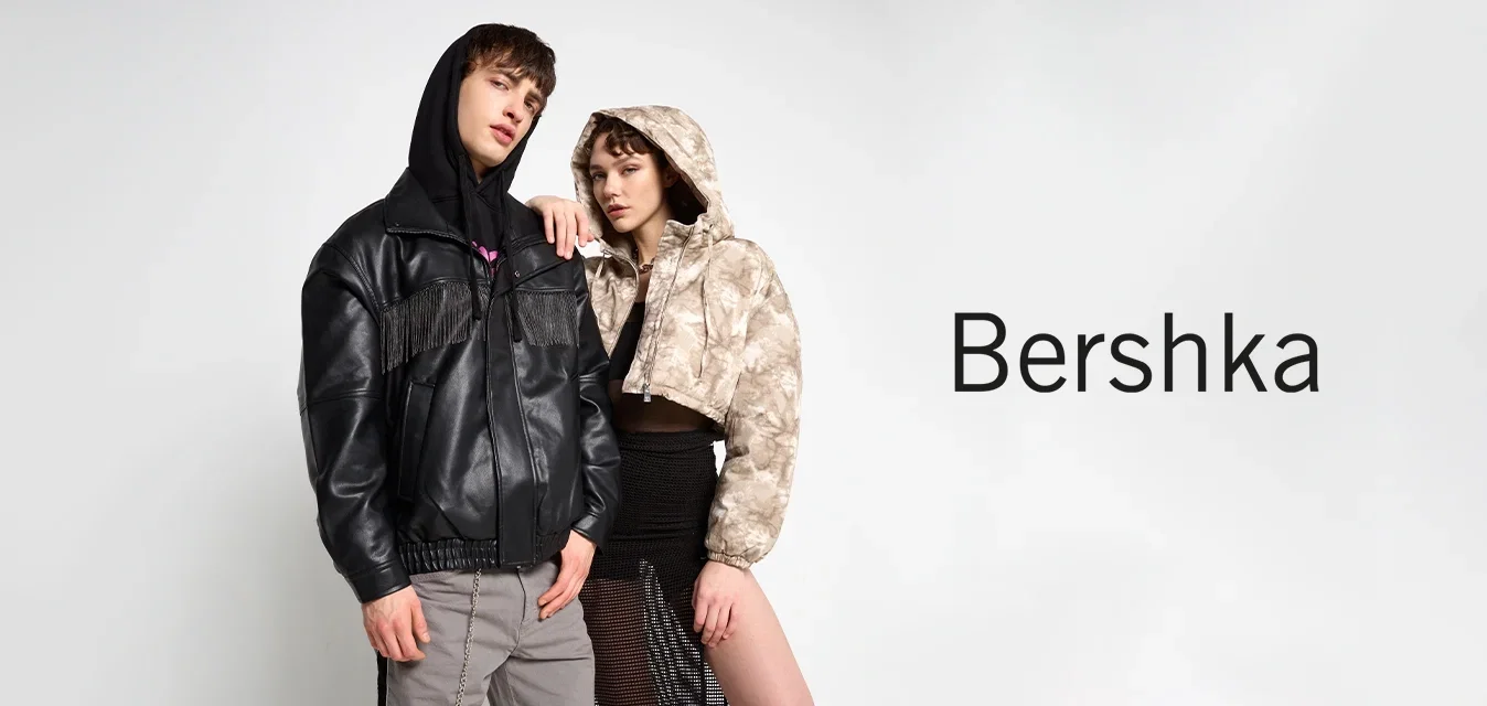 Schwarze Lederjacke mit Fransendetails, graue Hose mit Seitenkette und ein hellbrauner Camouflage-Cropped-Hoodie über einem schwarzen Netzrock.