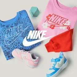 Gefaltete blaue und pinke Nike-Sweatshirts mit Logo, zwei Kleinkind-Sneakers in Pink und Blau, rote und blaue geometrische Blöcke auf beigem Hintergrund.