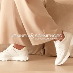 Beige Anzugensemble mit locker sitzendem Blazer und weitem Hosenbein, kombiniert mit weißen Sneakern. Präsentiert in einem minimalistischen, neutral gehaltenen Raum.