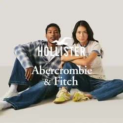 Zwei junge Erwachsene sitzen auf dem Boden, tragen legere Jeans und Turnschuhe und schauen mit entspannten Gesichtsausdrücken nach vorne vor einem einfarbigen Hintergrund.
