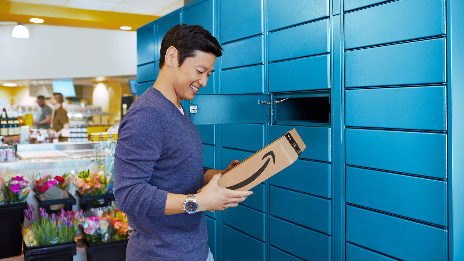 A man holds an Amazon parcel beside an open blue pickup locker