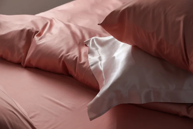 A close-up view of a bed with pink silk linens and pillowcases