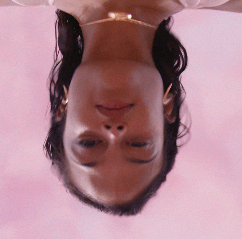 A model stares at their reflection through ripples of pink water.