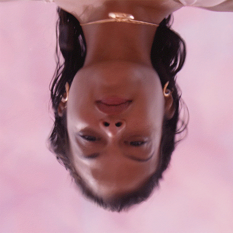 A model stares at their reflection through ripples of pink water.