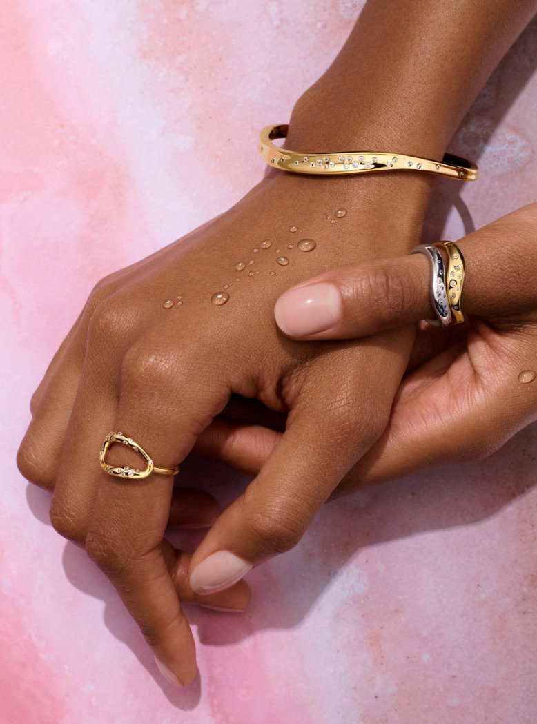 A pair of hands wear 14k gold-plated rings and bangle.