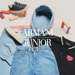Hellblaue Kapuzenjacke, schwarzes Poloshirt mit rotem Logo, blaue Jeans und drei Paar bunte Kindersneaker rund um die Kleidung auf weißer Oberfläche.