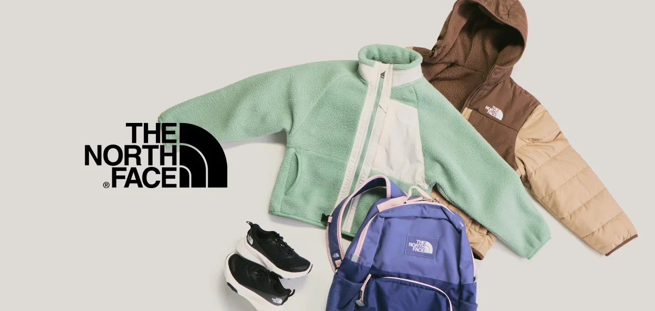 Grüne Fleecejacket, braune und beige Steppjacke, blauer Rucksack und schwarze Sportschuhe auf hellem Hintergrund angeordnet.