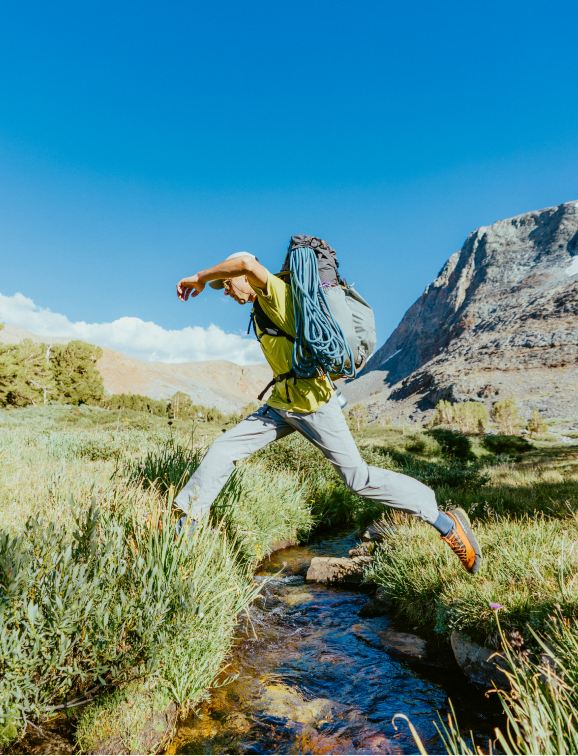 A hiker jumping over a stream