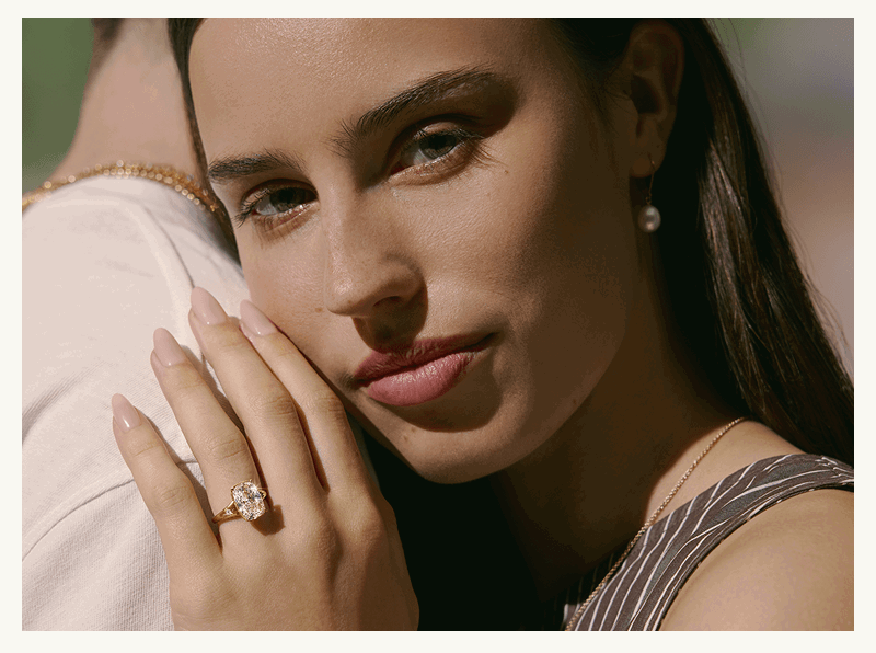 Model learning on partner, with cushion-cut diamond ring & pearl drop earring.