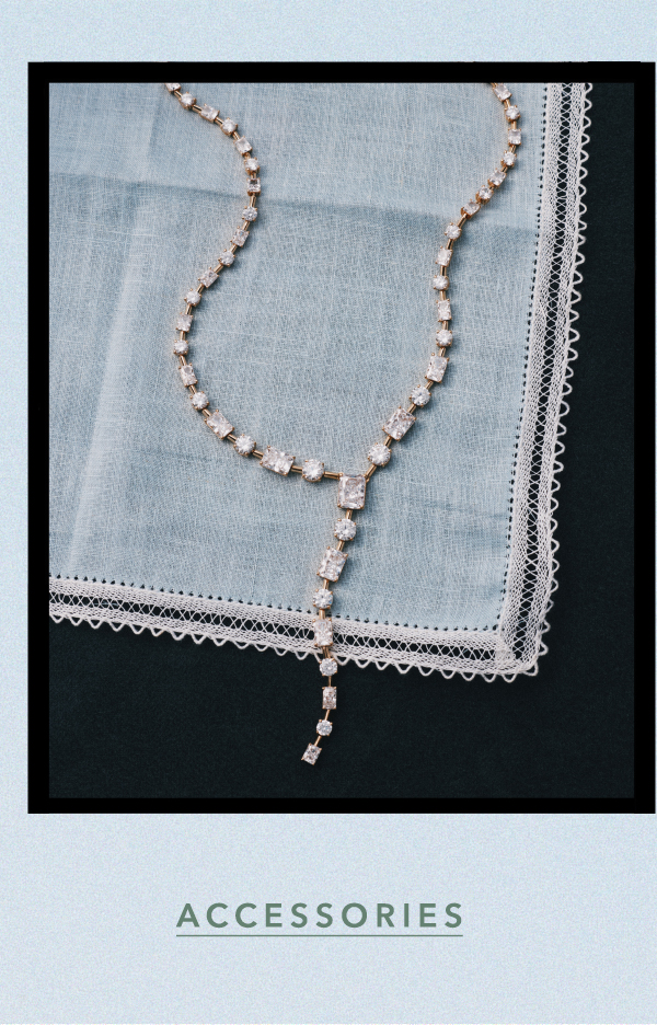 Sparkling crystal lariat necklace displayed on a light blue lace-trimmed handkerchief against a dark background. Text: ACCESSORIES.