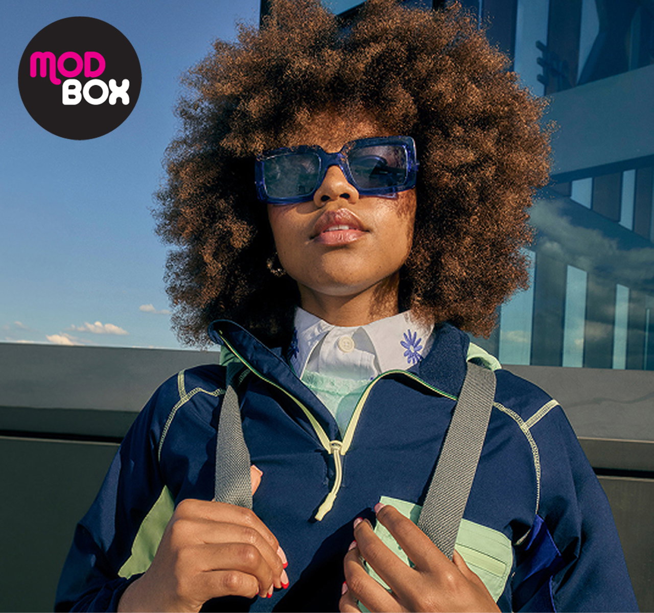 A model with an afro wearing sunglasses and a navy jacket 
