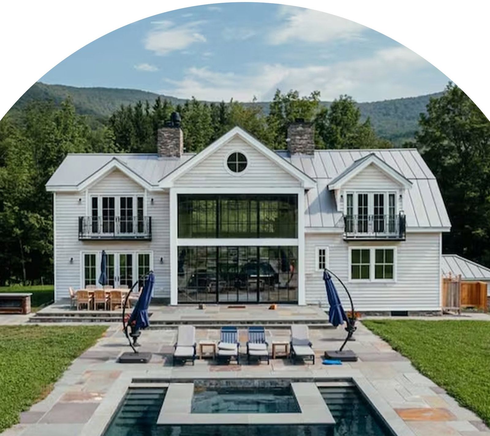 White country-style home with pool, patio seating, and mountain backdrop.