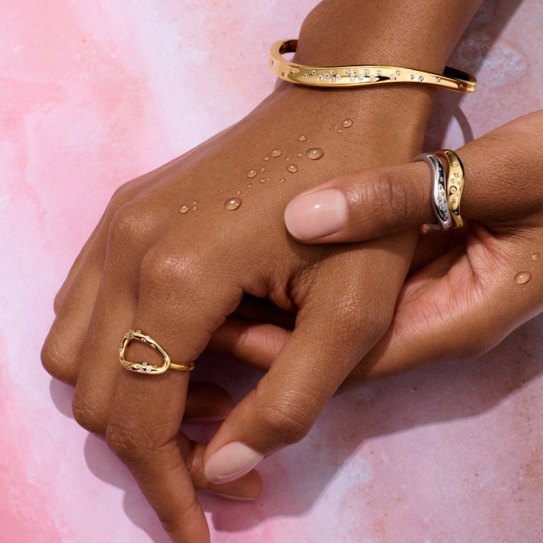 A pair of hands wear 14k gold-plated rings and bangle.