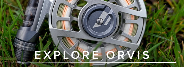 Explore Orvis - a close up of a fishing reel, attached to a fishing rod, lying in a patch of green grass