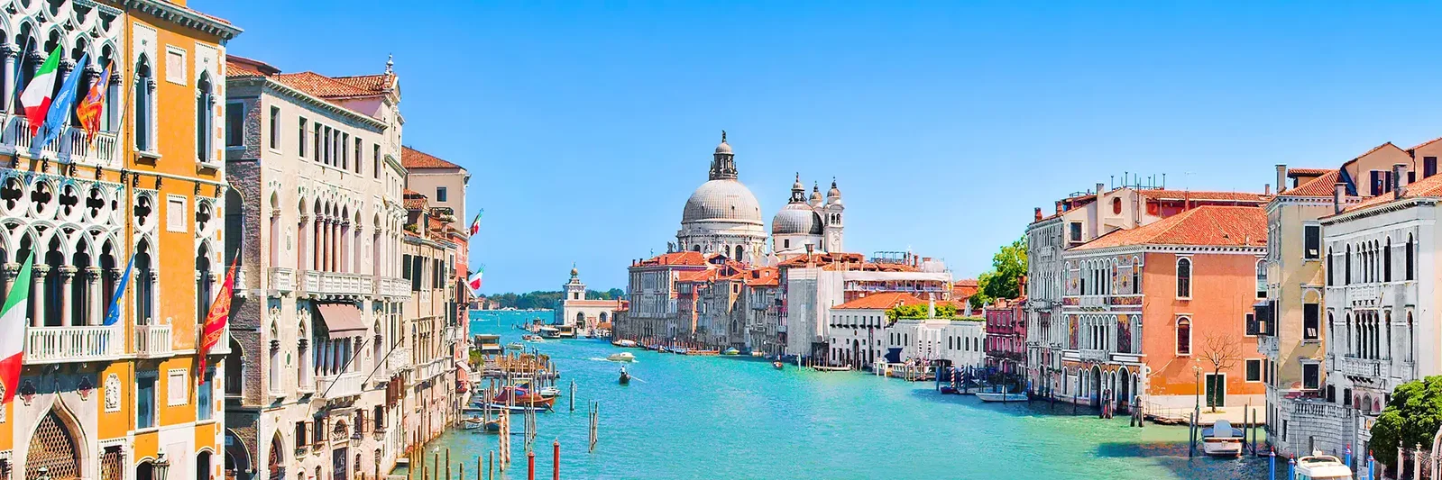 A scenic view of colourful buildings lining a canal in Venice, with boats and a clear blue sky.