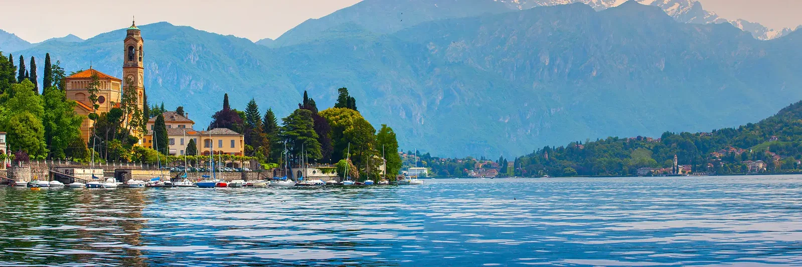 Scenic view of a lakeside village with mountains in the background and boats on the water.