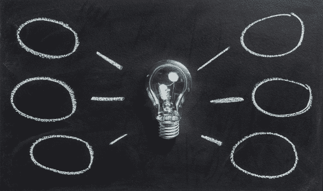 A clear lightbulb is centered on a black background with chalk-drawn lines and empty ovals radiating out, suggesting a brainstorming or mind mapping concept.
