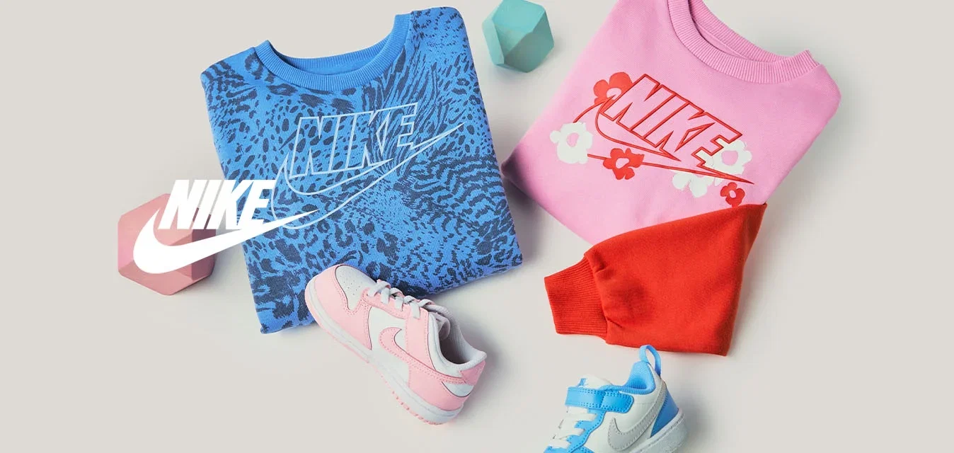 Gefaltete blaue und pinke Nike-Sweatshirts mit Logo, zwei Kleinkind-Sneakers in Pink und Blau, rote und blaue geometrische Blöcke auf beigem Hintergrund.
