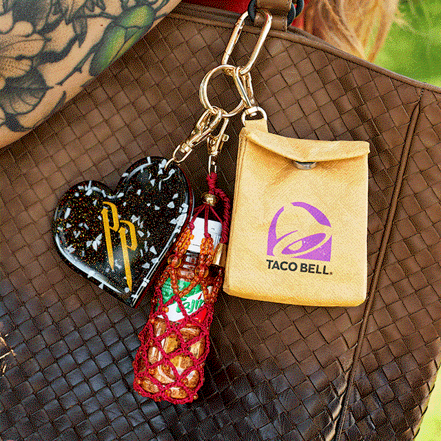 A bag charm set set including a Tajín bottle in a hand-beaded holder, a mini Taco Bell bag, and a heart charm featuring Peso Pluma’s logo.
