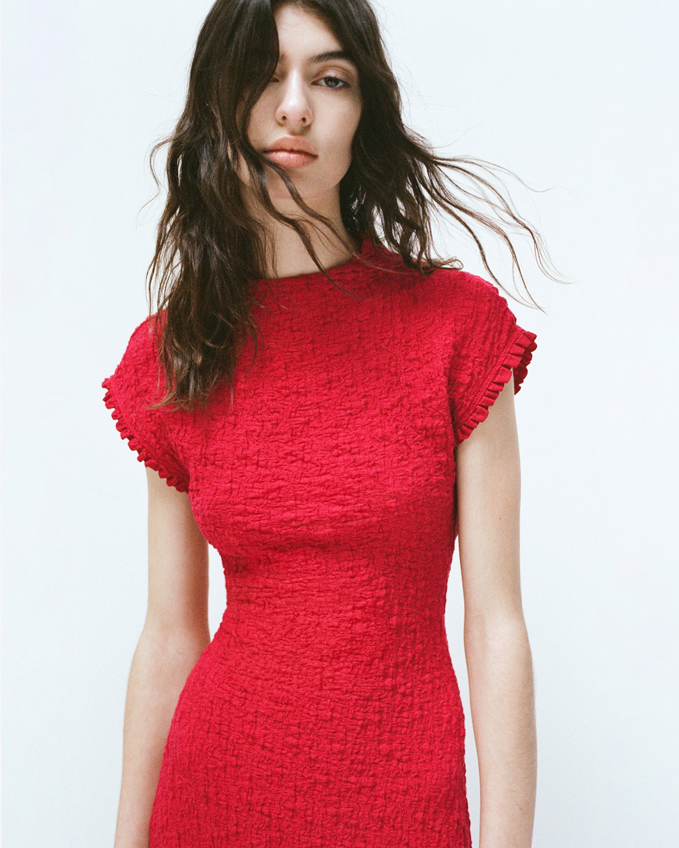Cropped image of model stading against white backgroudn wearing the Cleo Dress in Jersey Jacquard in red