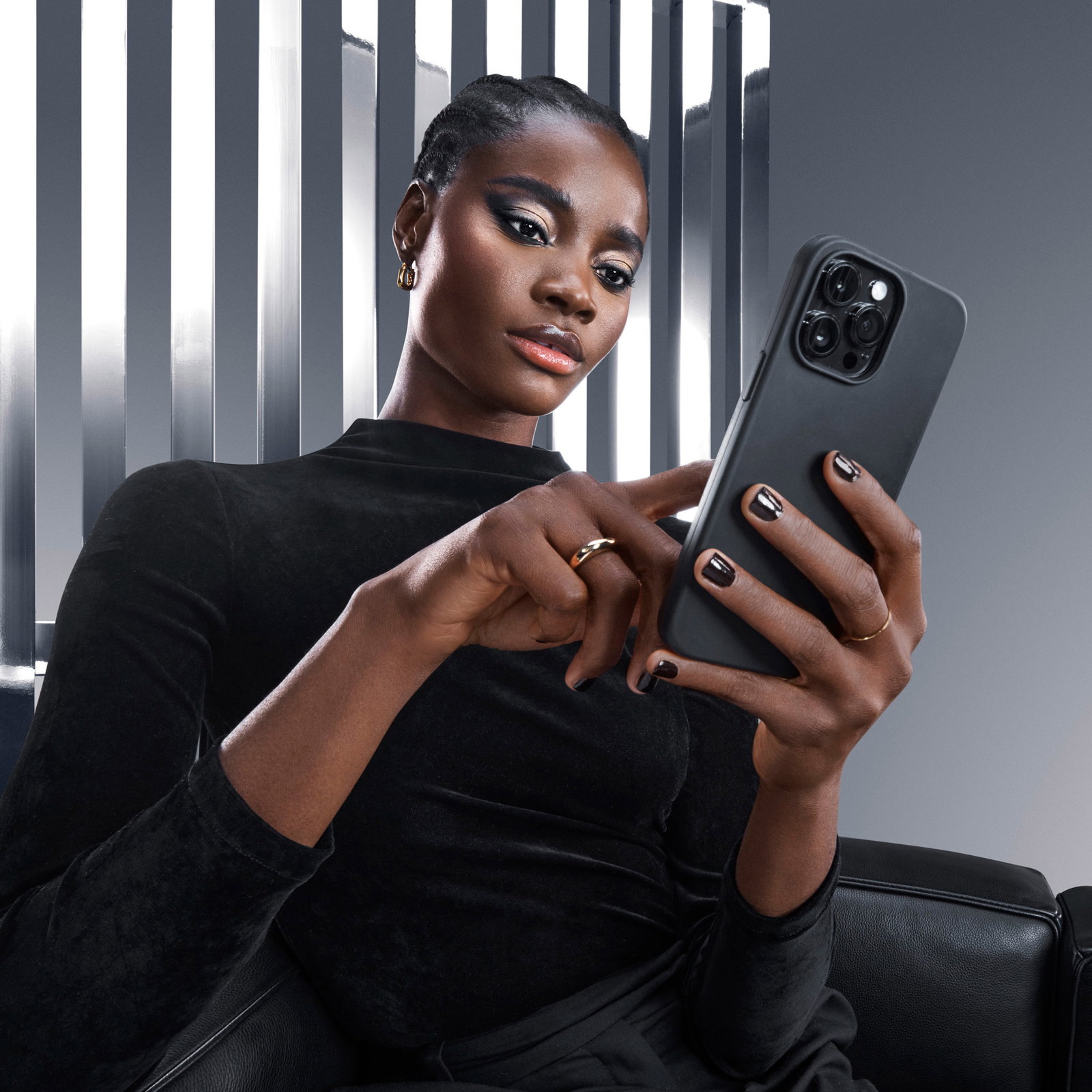 Elegant woman in black attire holding a smartphone in a sleek, modern setting.