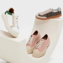 Legere Sneaker in Weiss mit grünen Akzenten, sanftem Pink und gewebten braunen Texturen, präsentiert auf einer weißen, geschwungenen Plattform.