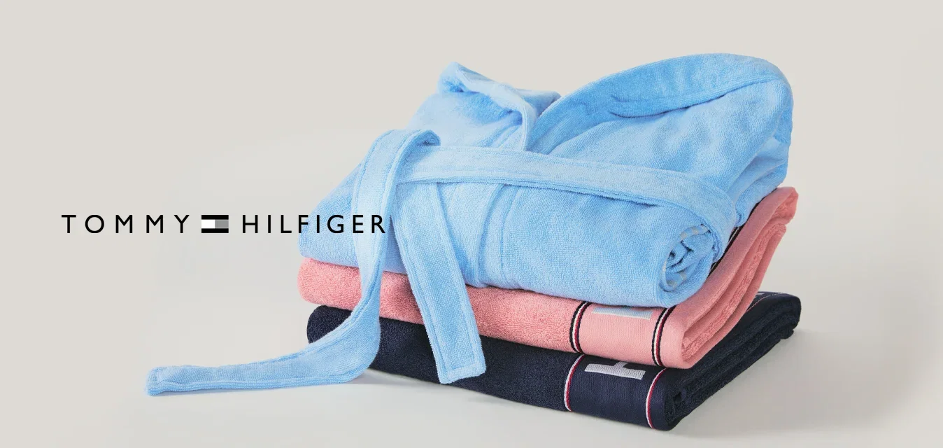Stapel von drei gefalteten Roben in Blau, Pink und Dunkelblau mit einem gebundenen Gürtel auf hellem Hintergrund.