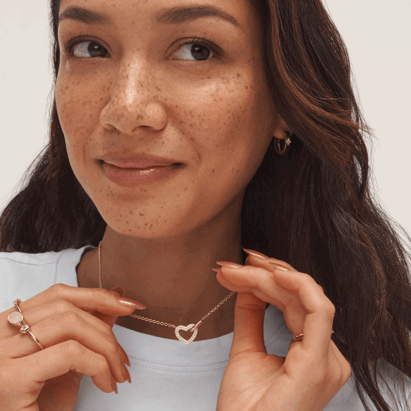 Woman wearing a yellow gold open-heart diamond necklace, gold earrings and fashion rings.