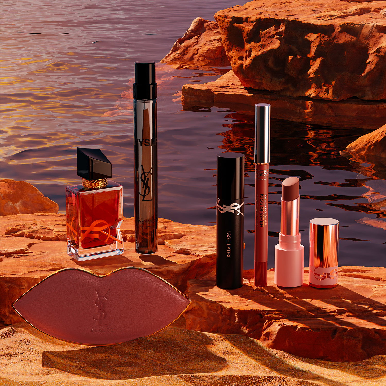 A selection of YSL beauty products, including perfume, mascara, lipstick, and a lip-shaped compact, arranged on red rocks by the water.