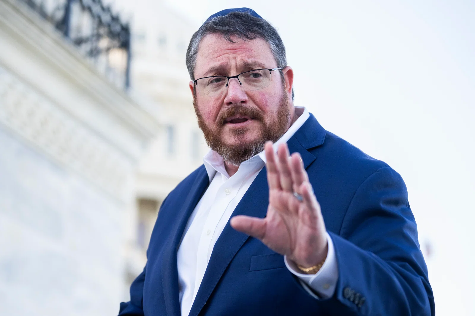 Randy Fine, Republican Senate hopeful, in a blue suit and glasses, gesturing during a speech.