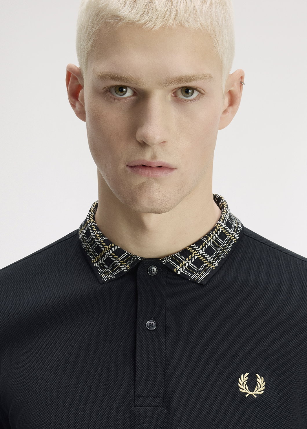 Introducing the Only At Fred Perry collection: model in the photo wears a black polo shirt with a contrast collar in our unique black/champagne registered tartan