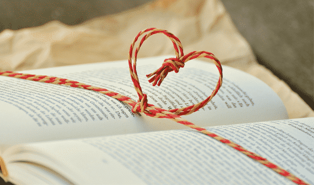 An open book with a red and white striped cord shaped into a heart resting on its pages.