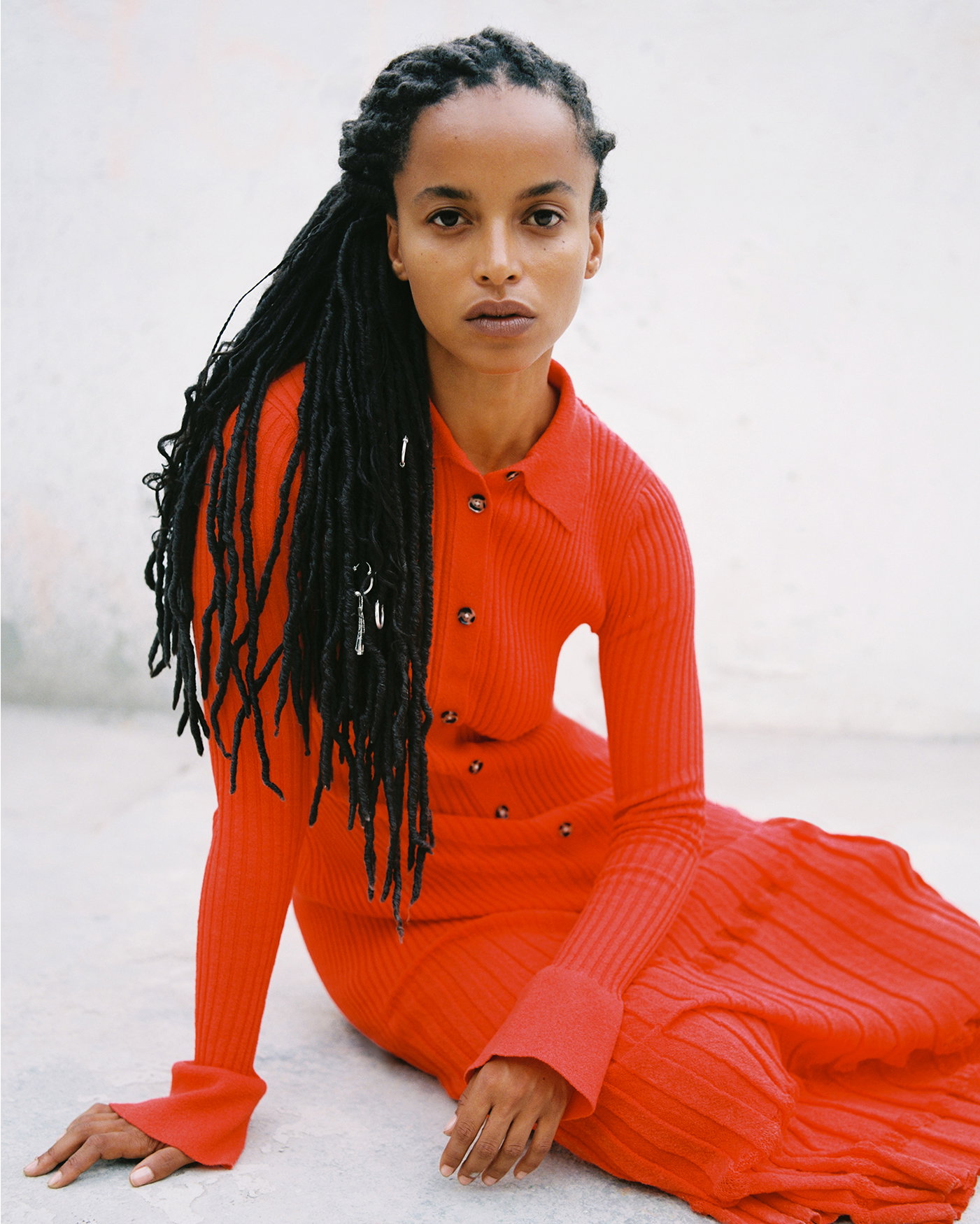 Image of model sitting across the floor wearing the Rosario Dress in Textured Merino Wool in Orange