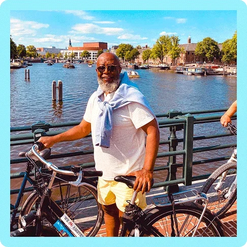 Image description: A man standing next to a bicycle along the canals in Amsterdam