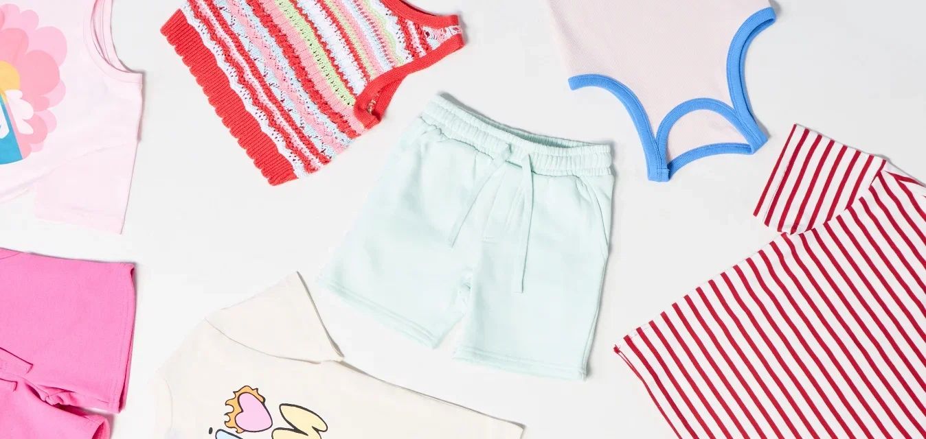 Verschiedene Kinderbekleidung umfasst eine gestreifte Weste, pastellfarbene Shorts, bedruckte T-Shirts und florale Shorts in verschiedenen Farben und Mustern.