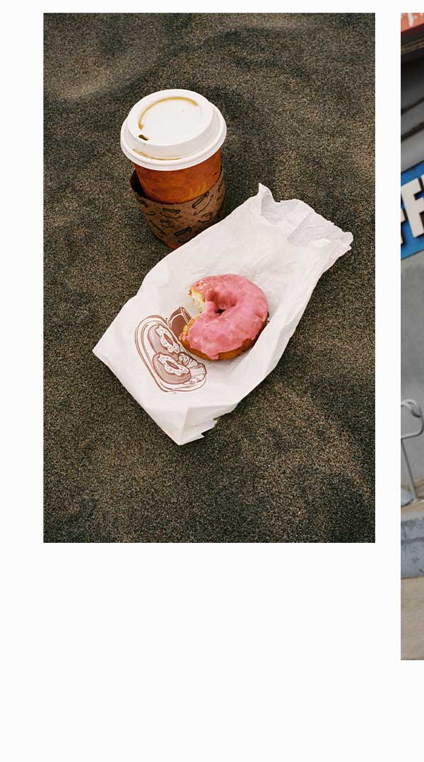 Half eaten donut on beach with coffee.