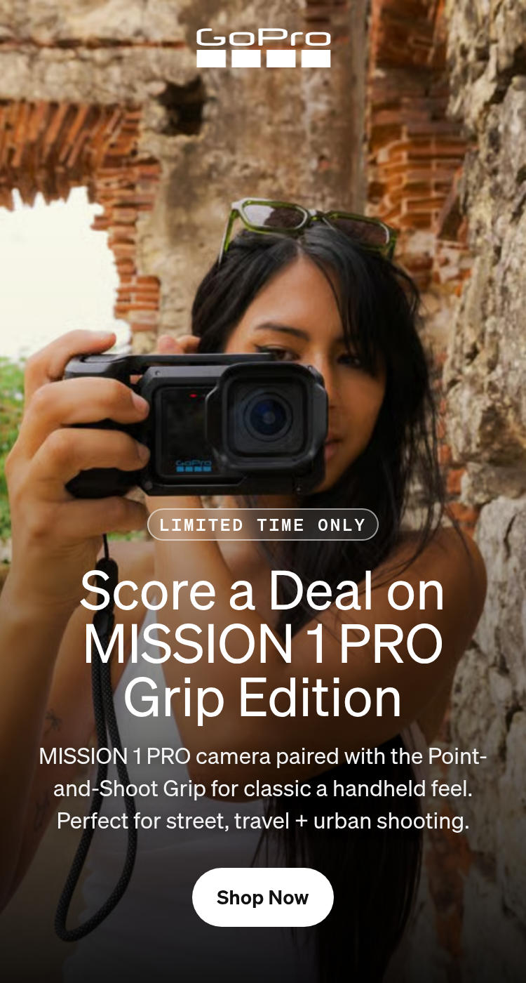 A woman holding a GoPro camera against an ancient stone wall.