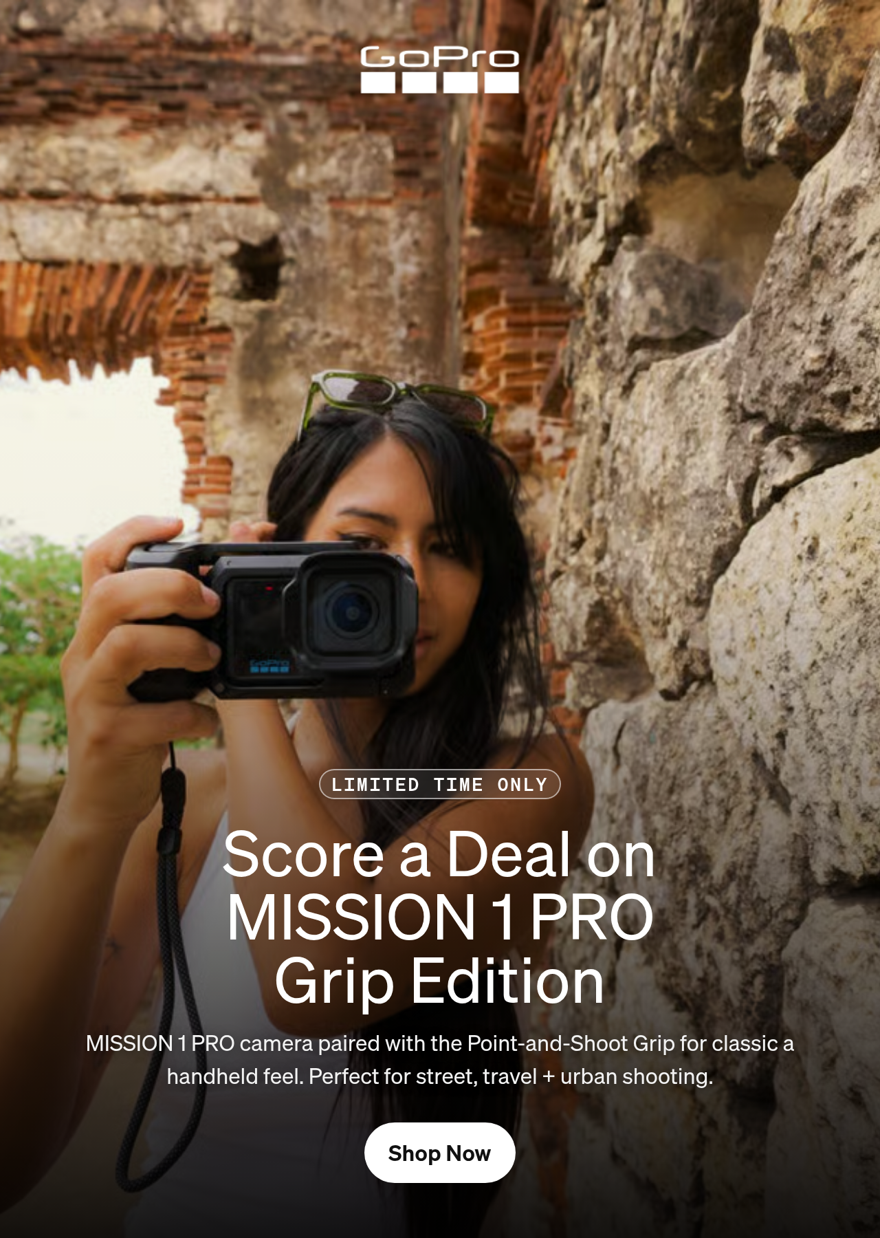 A woman holding a GoPro camera against an ancient stone wall.
