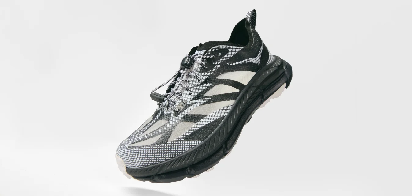 Schwarzer und grauer Sportschuh mit gemustertem Mesh-Obermaterial, mit gesicherten Schnürsenkeln und dicker gepolsterter Sohle, schräg auf einem weißen Hintergrund abgebildet.