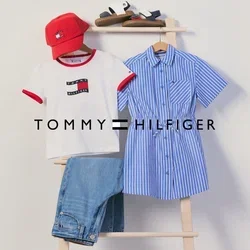 Rote Kappe, weißes T-Shirt, blaue Jeans, blau gestreiftes Kleid und Sandalen auf einer Holzleiter vor einer schlichten Wand ausgestellt.