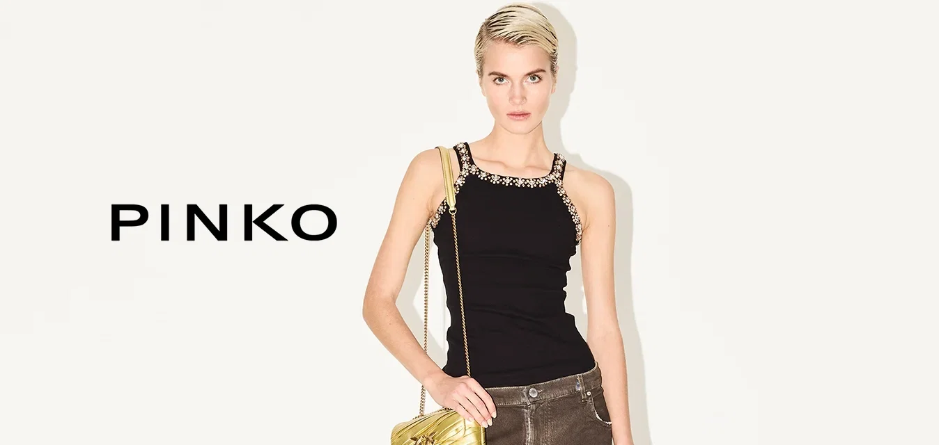 Schwarzes Tanktop mit dekorativen Trägern, braune weite Jeans mit hochgekrempelten Säumen und eine goldene Handtasche. Schwarze, geschnürte High Heels runden das Outfit ab.