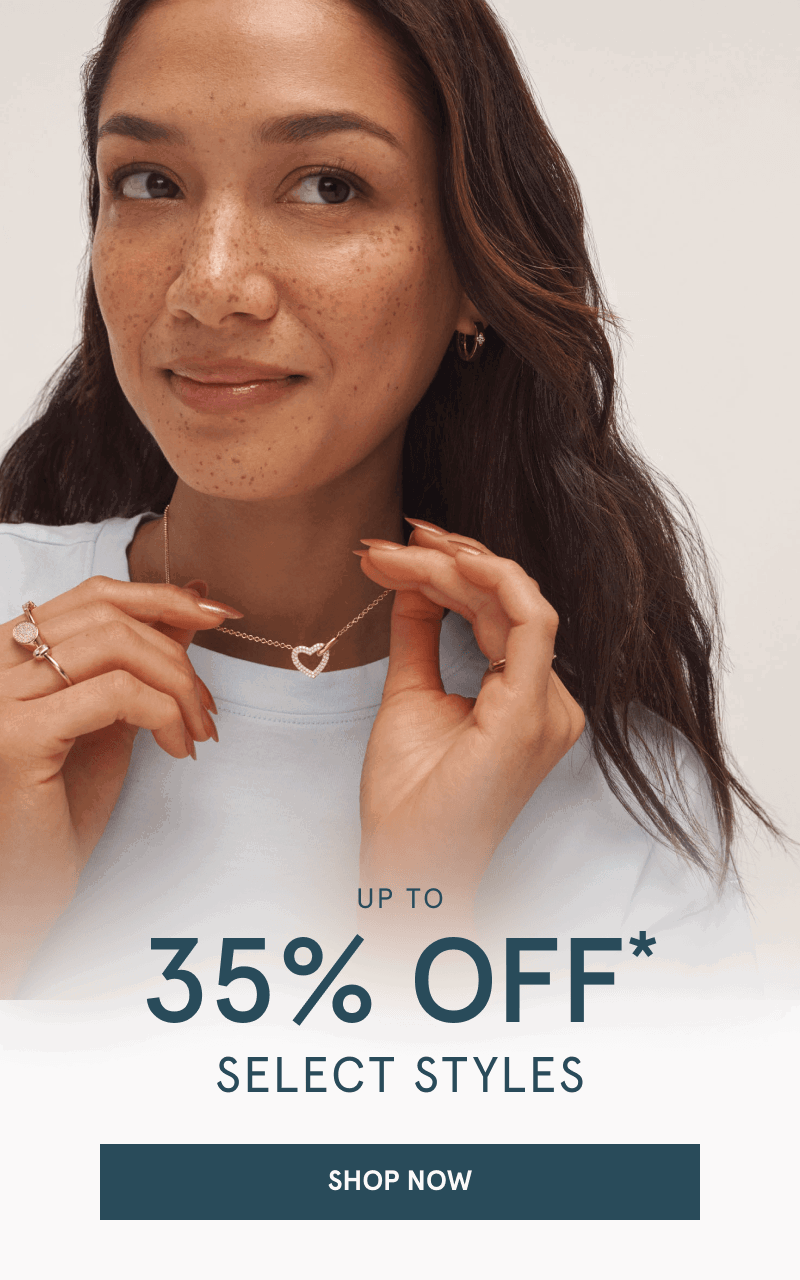 Woman wearing a heart pendant necklace, gold hoop earrings and gold rings. Up to 35% OFF select styles. Click shop now.